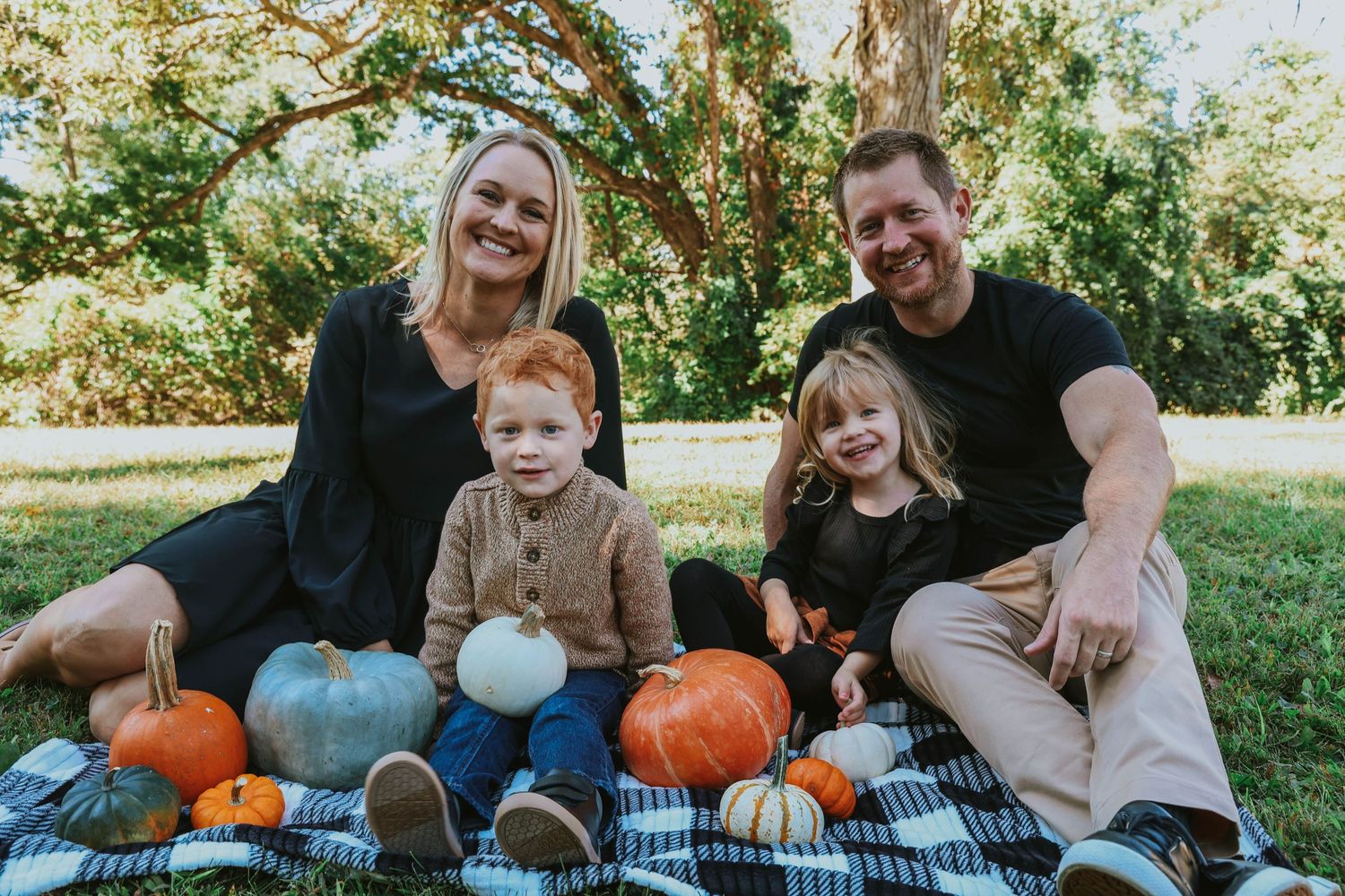 Family sitting on blanket with pumpkins during autumn outdoor photoshoot.