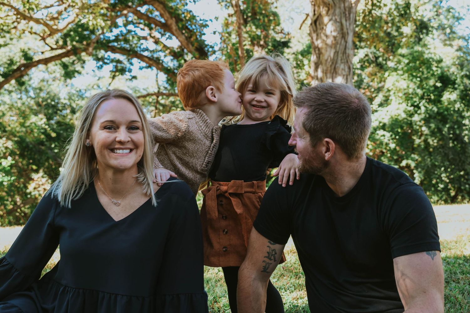 Joyful outdoor family portrait with lifting and laughter among trees.