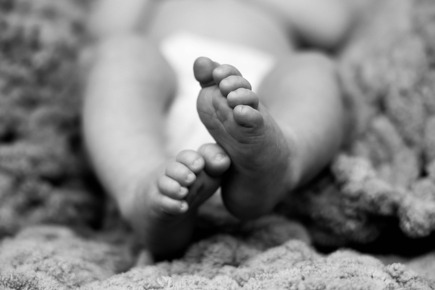 Close-up black and white photo of tiny baby feet on sandy texture.