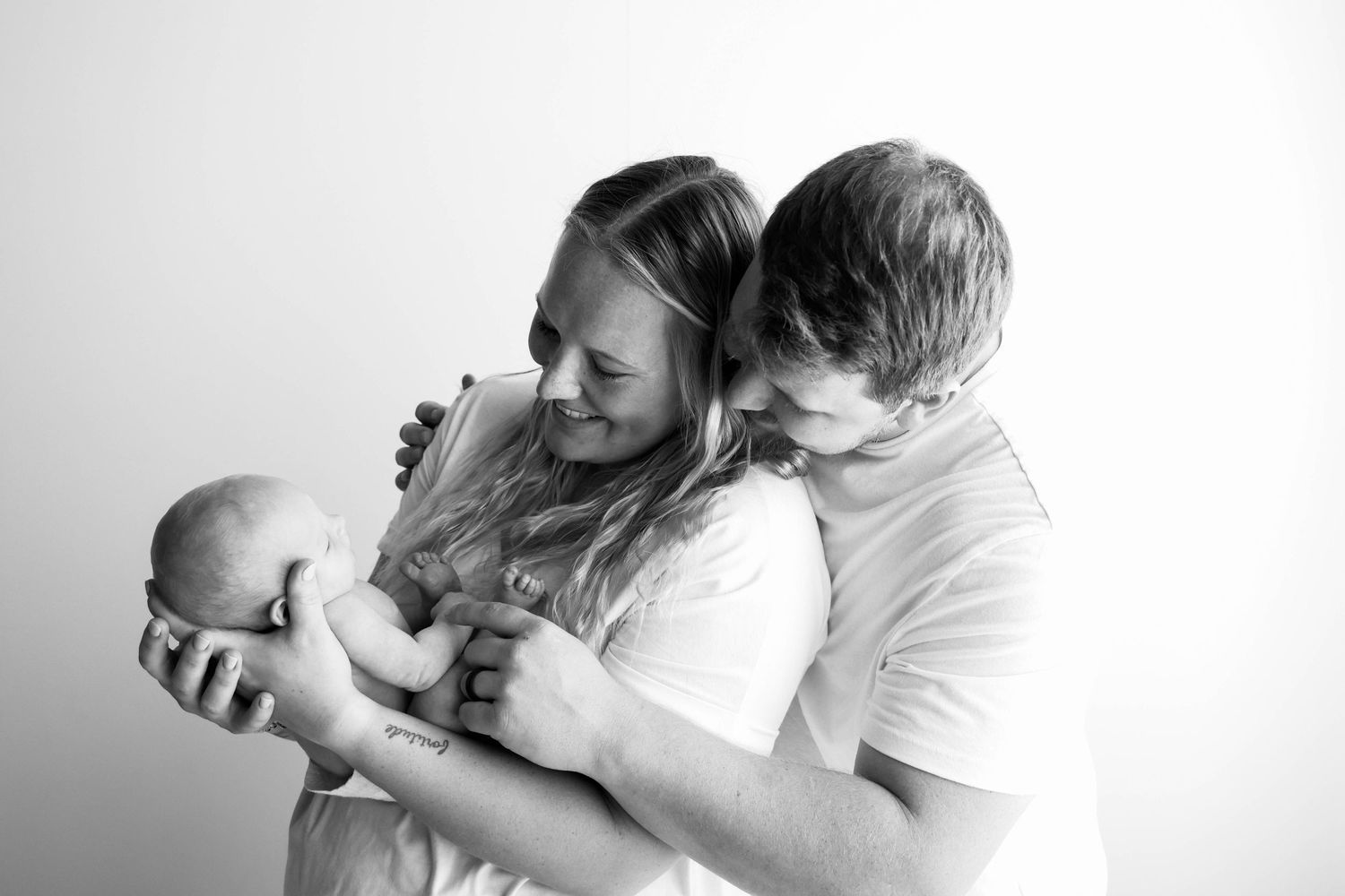 New parents sharing a tender moment with their newborn baby in black and white.