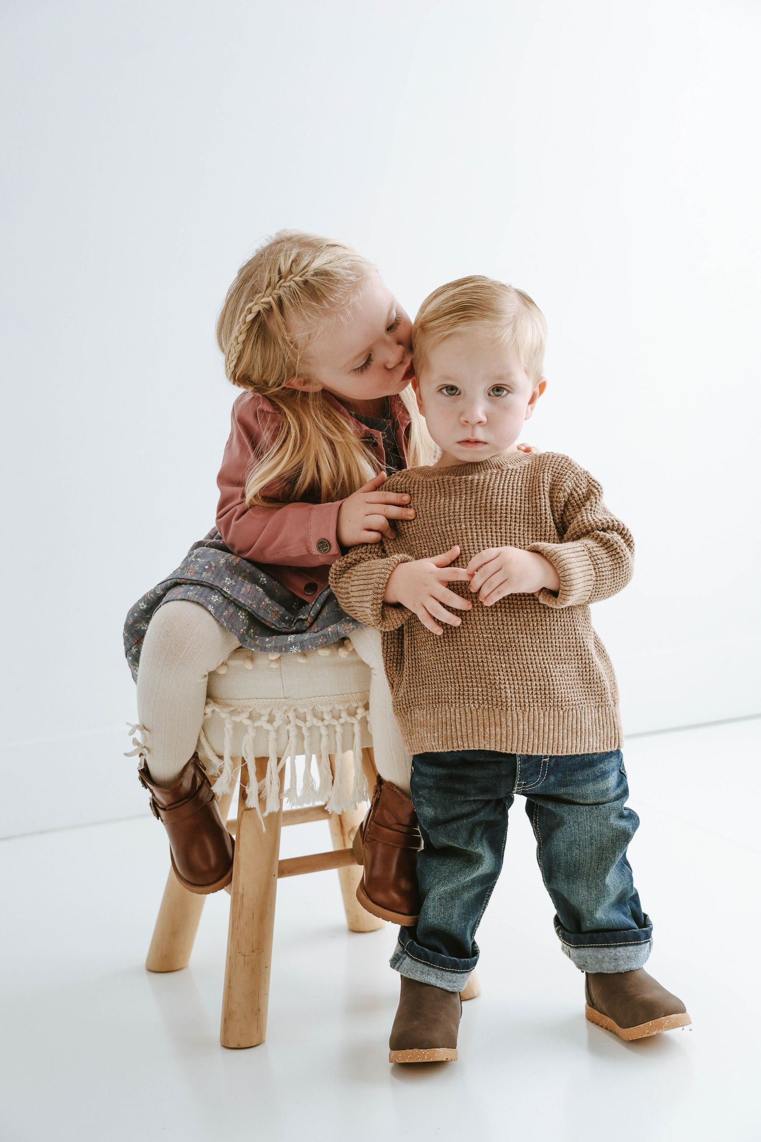 Two children sharing a sweet moment on wooden stool against white background.