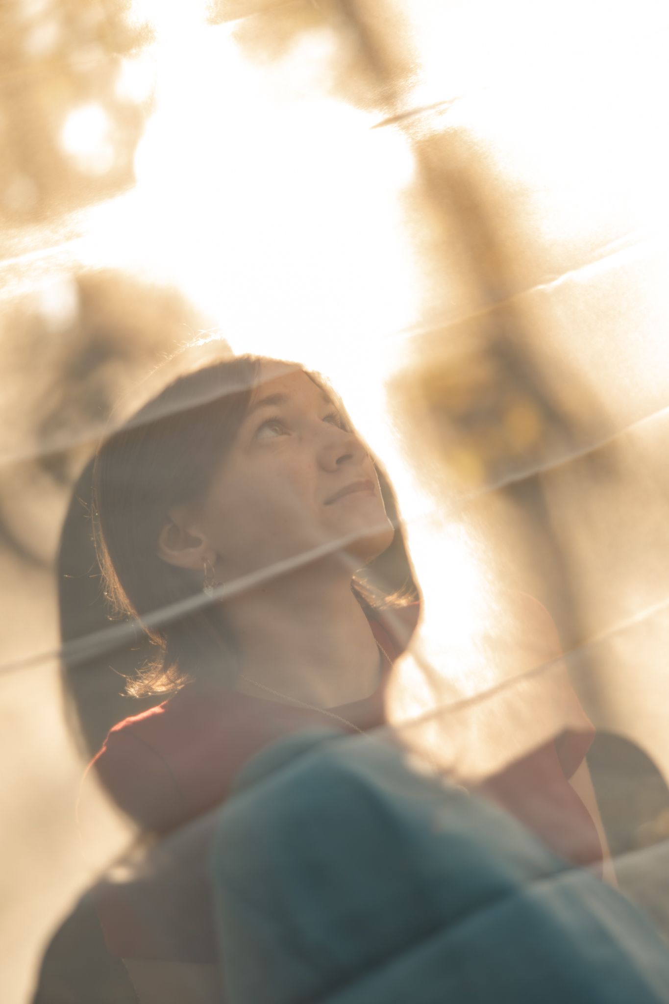 Person in teal sweater looking up with dreamy expression against soft blurred background in warm lighting.