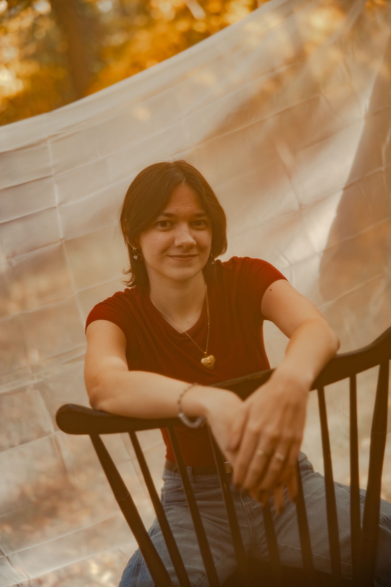 A dreamy portrait in warm tones shows someone seated in a wooden chair against a white backdrop with autumn colors behind.