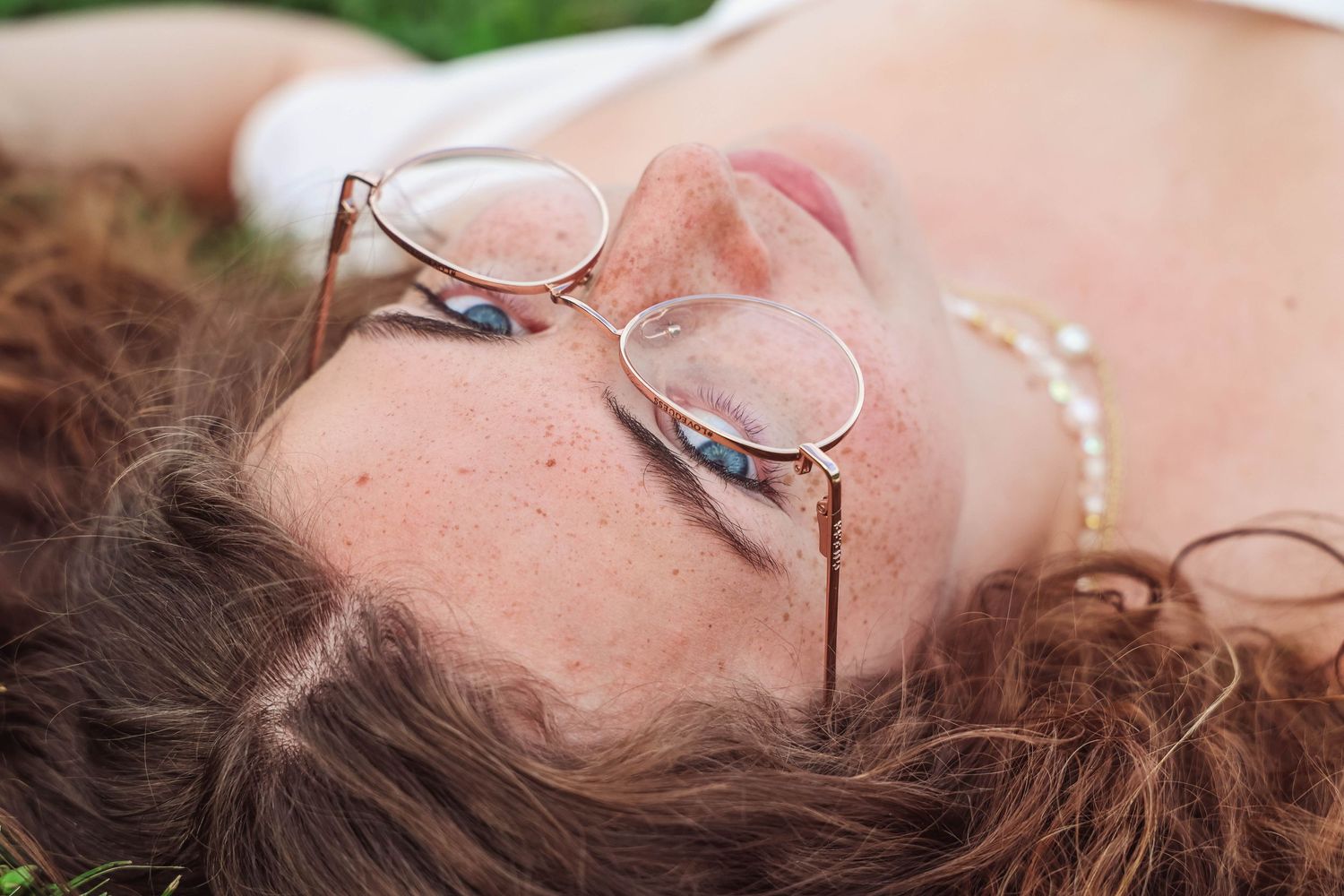 A close-up overhead shot of someone lying down wearing round glasses with curly hair framing their face.