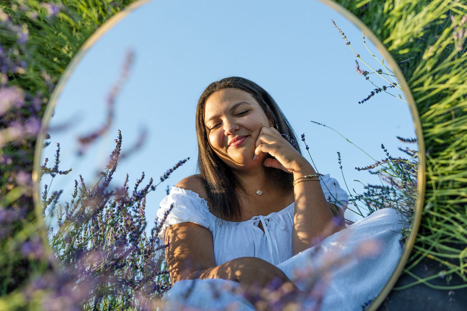 Dreamy summer portrait of a woman laying in lavender field with sun flare and mirror reflection composition.