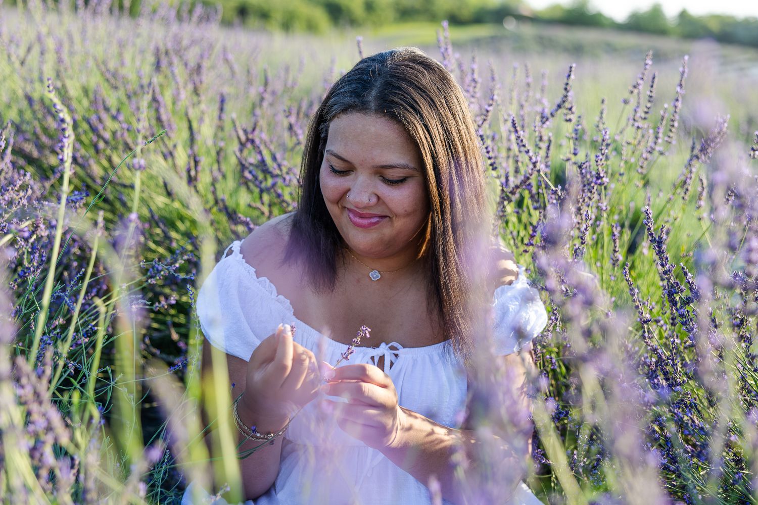 Woman in white dress walks through vibrant purple lavender field on sunny summer day.