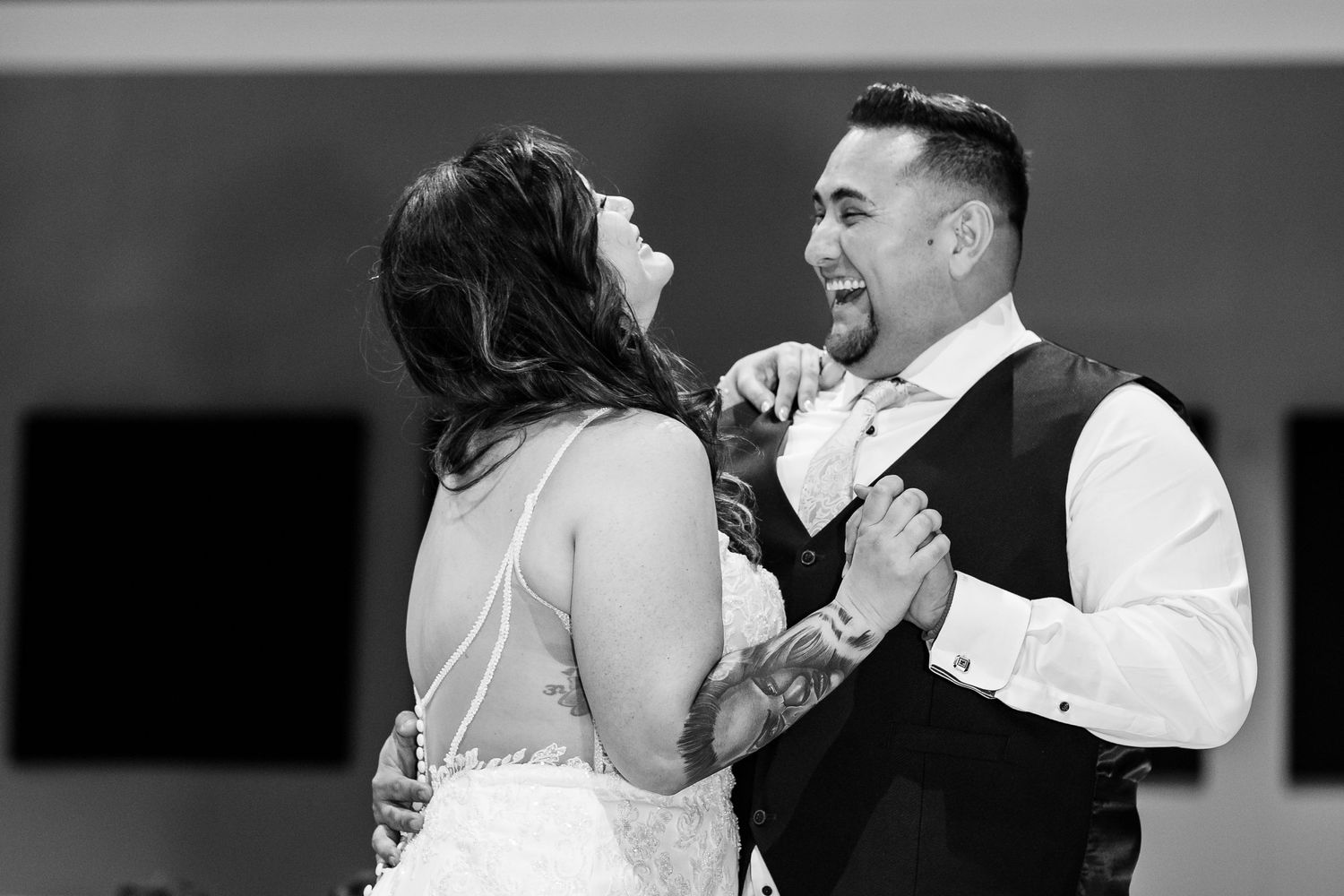 A joyful couple dances together at their wedding reception in black and white.