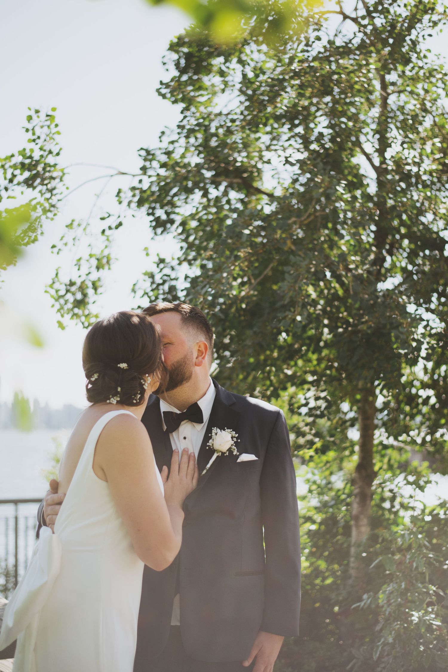 Intimate moment between newlyweds under trees with soft natural lighting.