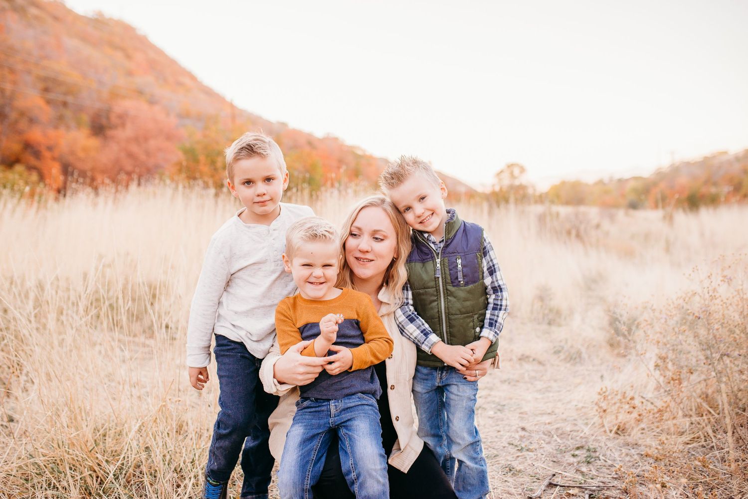 A family group sits together in tall golden grass with mountains in the background.