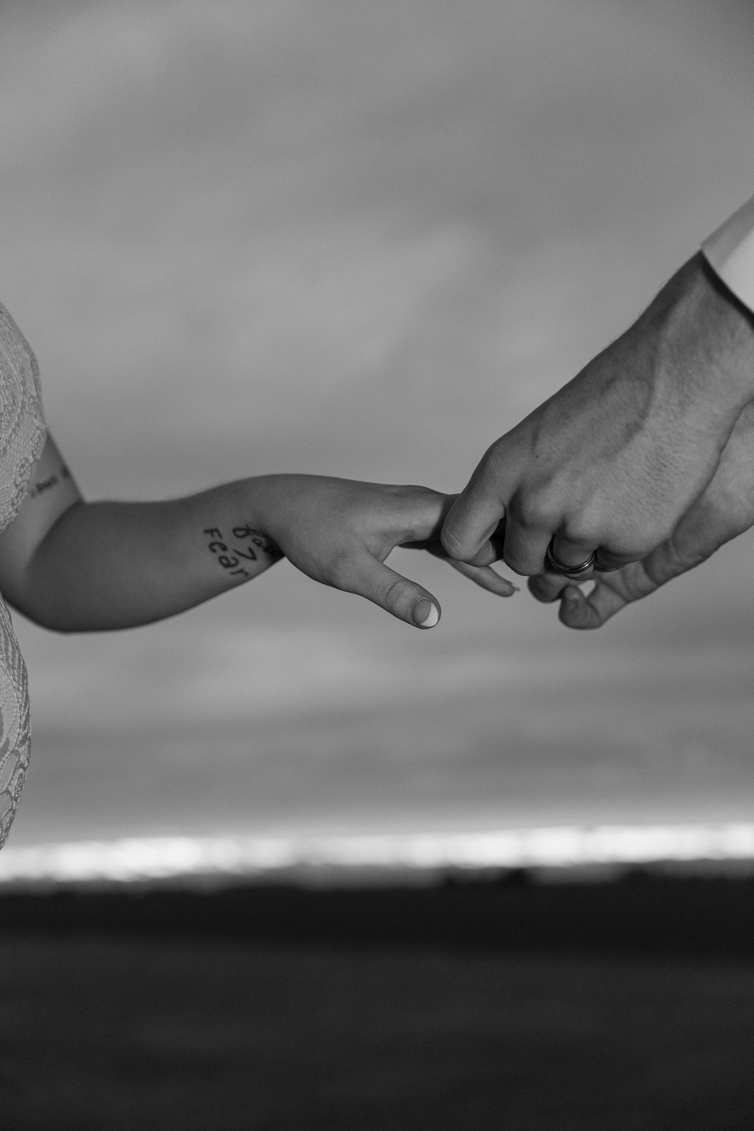 Silhouetted hands reaching toward each other against a misty horizon at sunset.