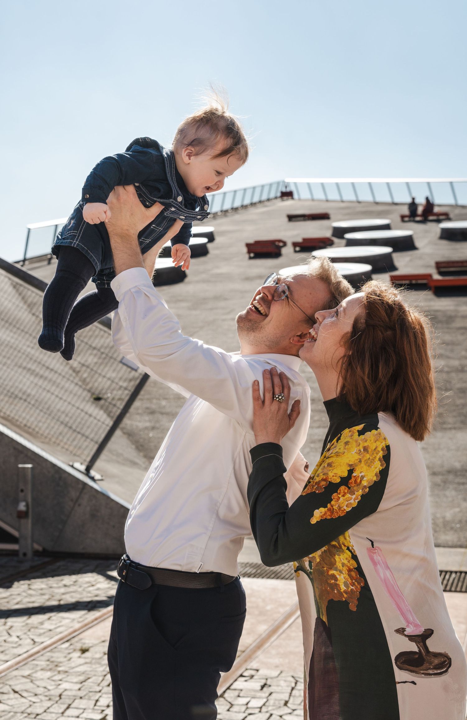 A joyful sequence of four photos showing a couple lifting and playing with a small child outdoors on a sunny day.