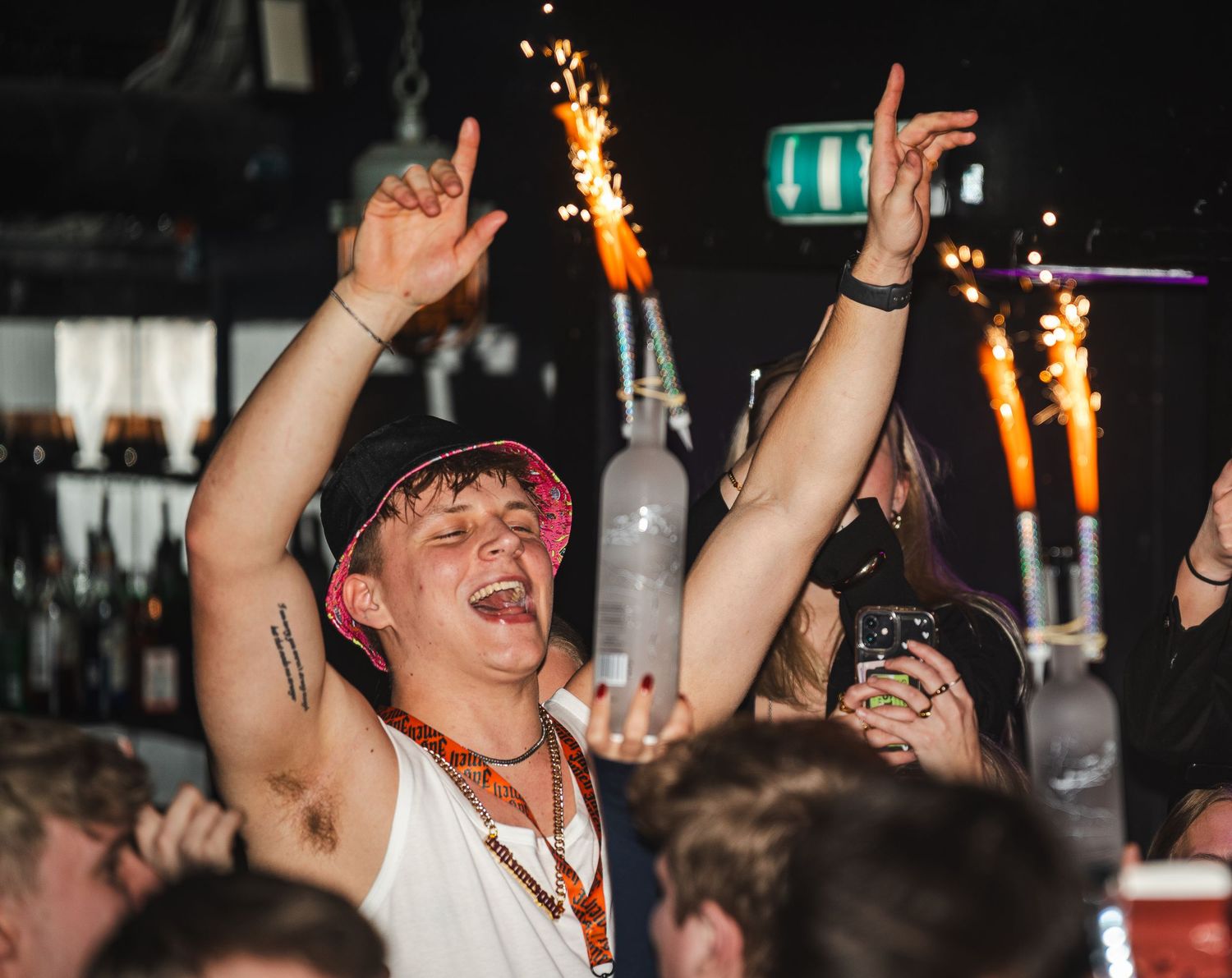 Enthusiastic concertgoer with arms raised celebrating at a nightclub with sparklers and lighting in the background.