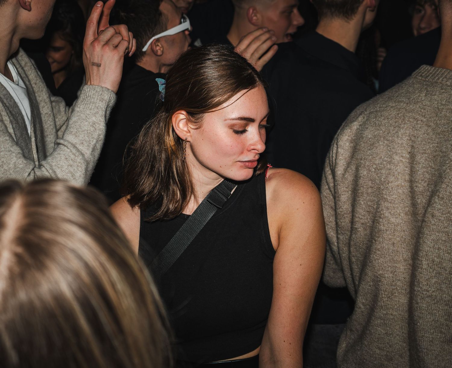 Person in black sleeveless top dancing at a crowded nightclub in dim lighting.