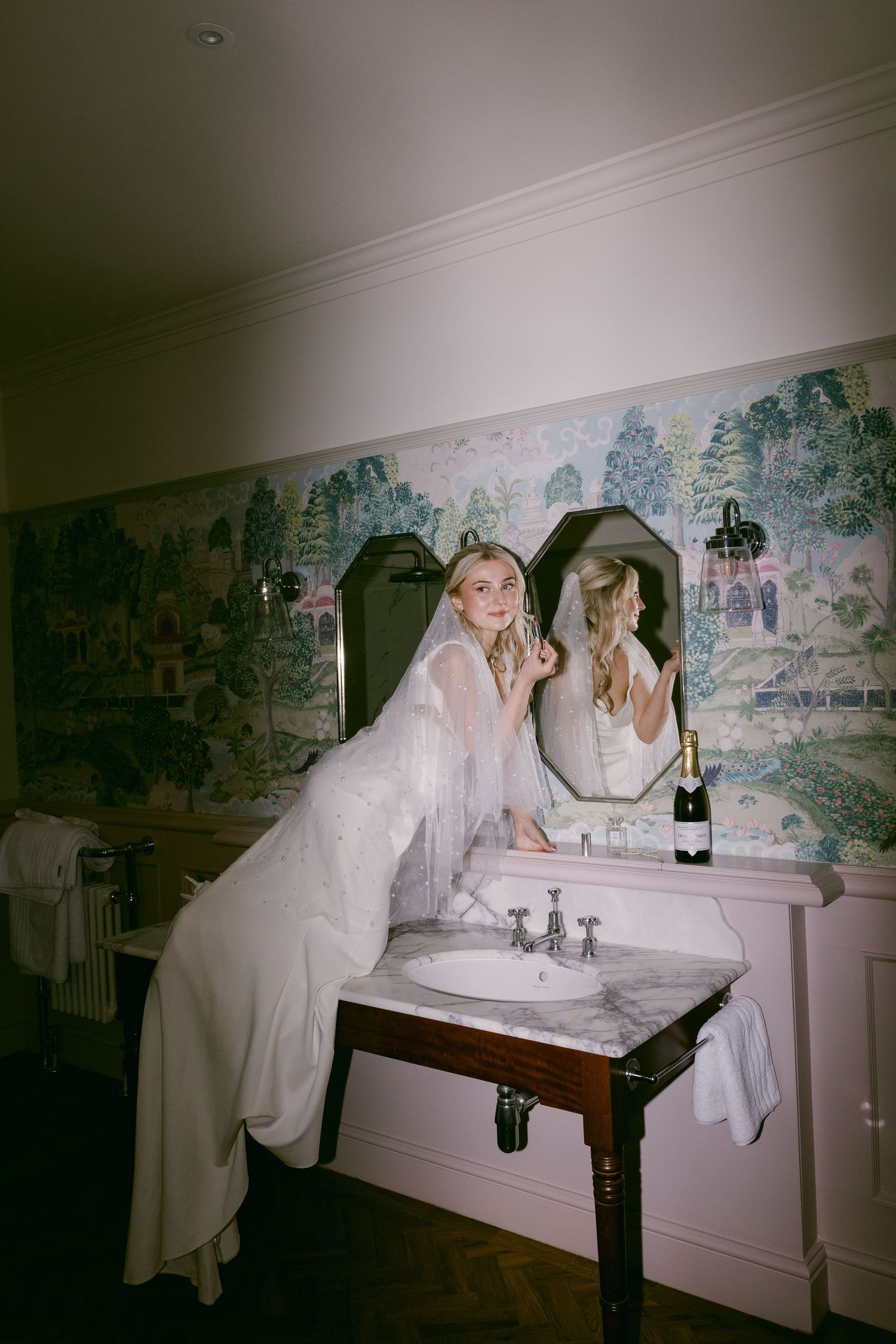 Night time flash photo of bride doing her make up while kneeling on sink in bathroom at Burtonfields Hall Yorkshire on wedding evening
