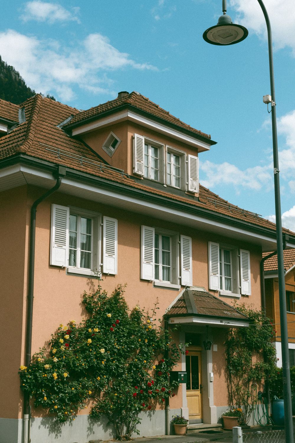 Peach-colored residential building with white shutters and orange climbing plants on the exterior wall under blue sky.