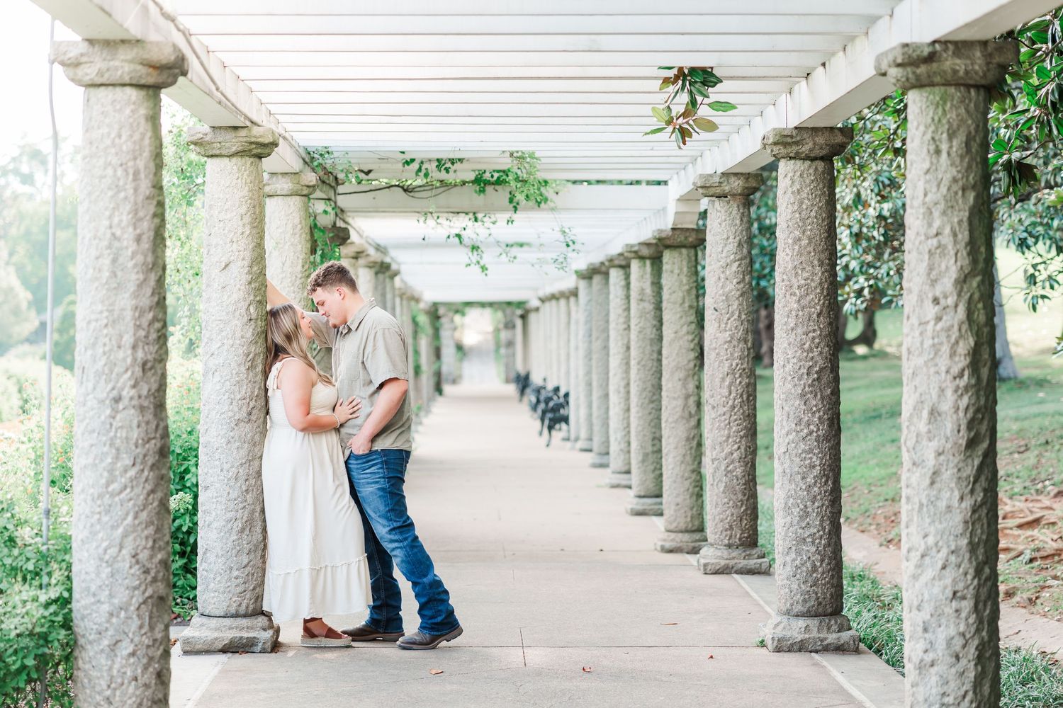 Romantic couple sharing moment in columned walkway with hanging greenery.