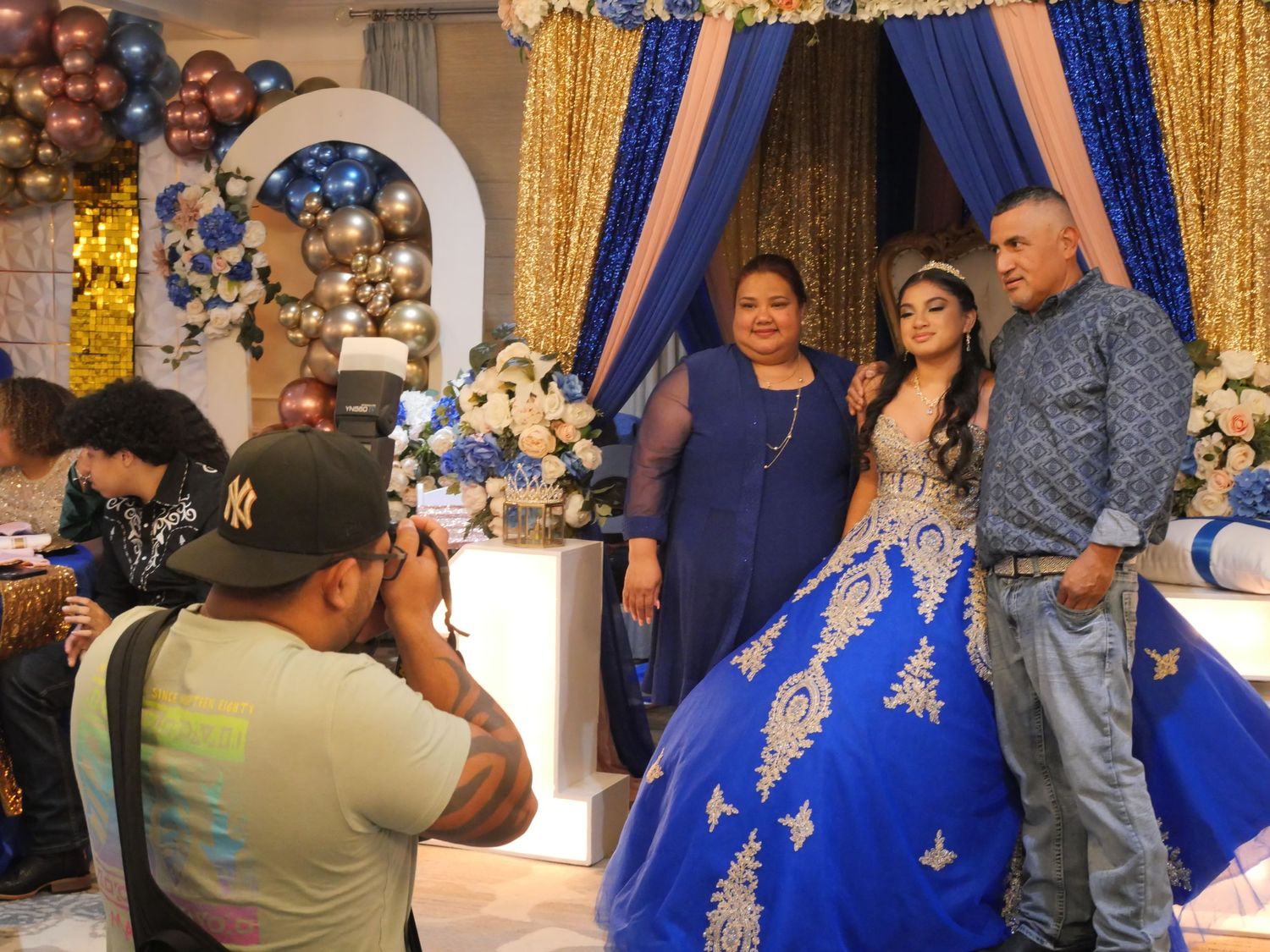 Behind-the-scenes shot of photographer capturing quinceañera celebration with blue and gold decor.