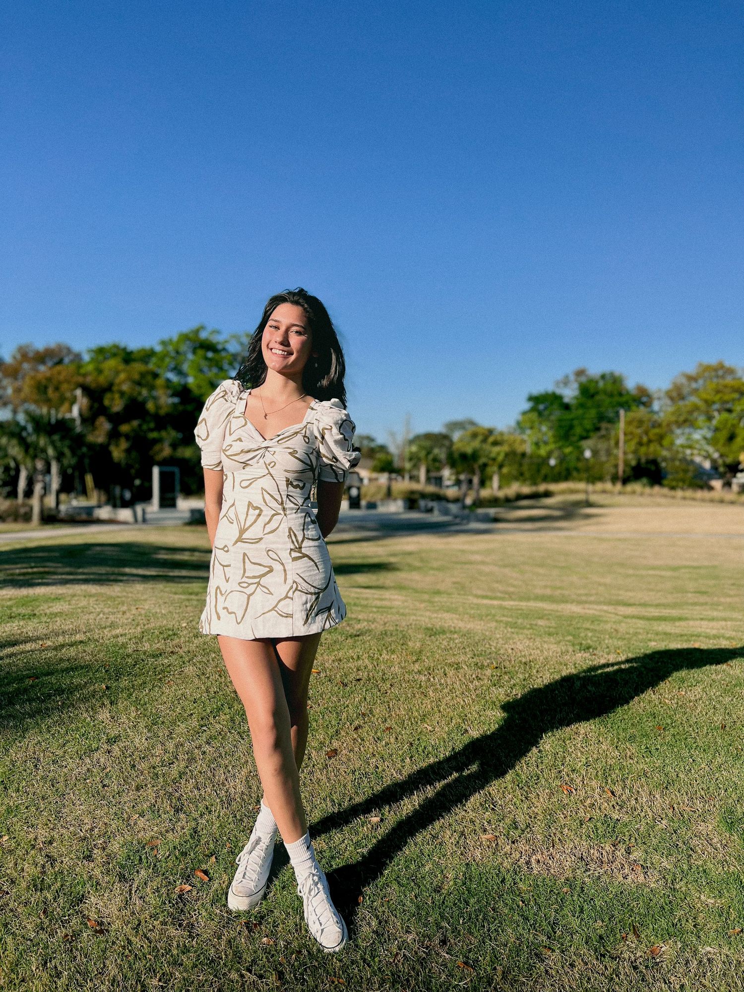 Person in patterned dress posing on grass with trees in background.