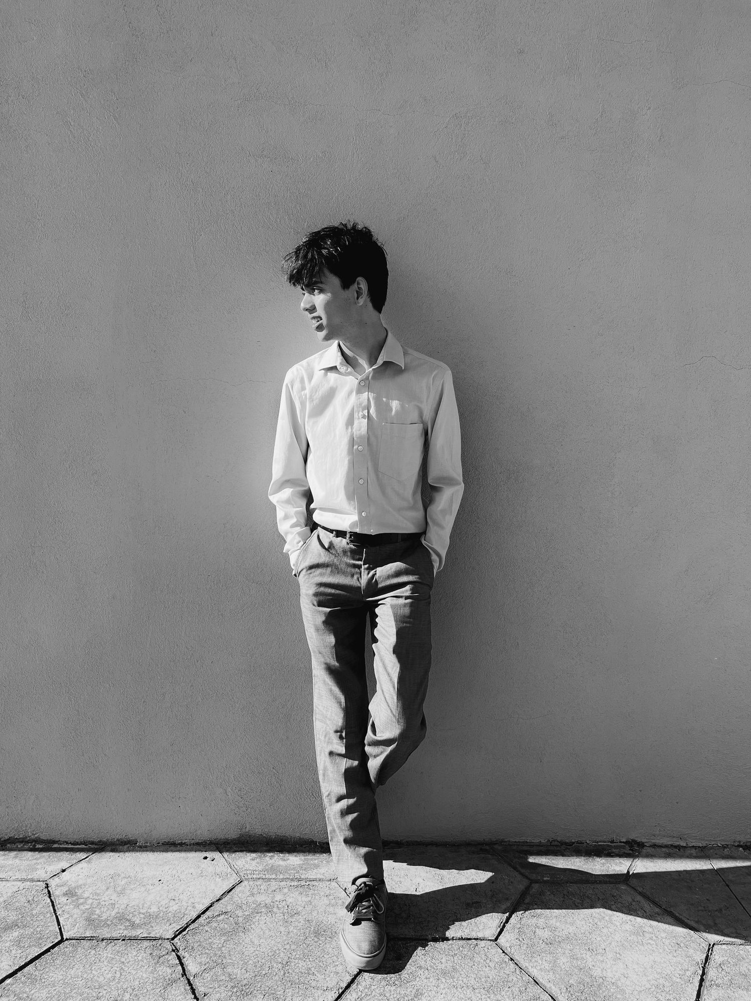 Black and white portrait of person leaning against wall in casual attire.