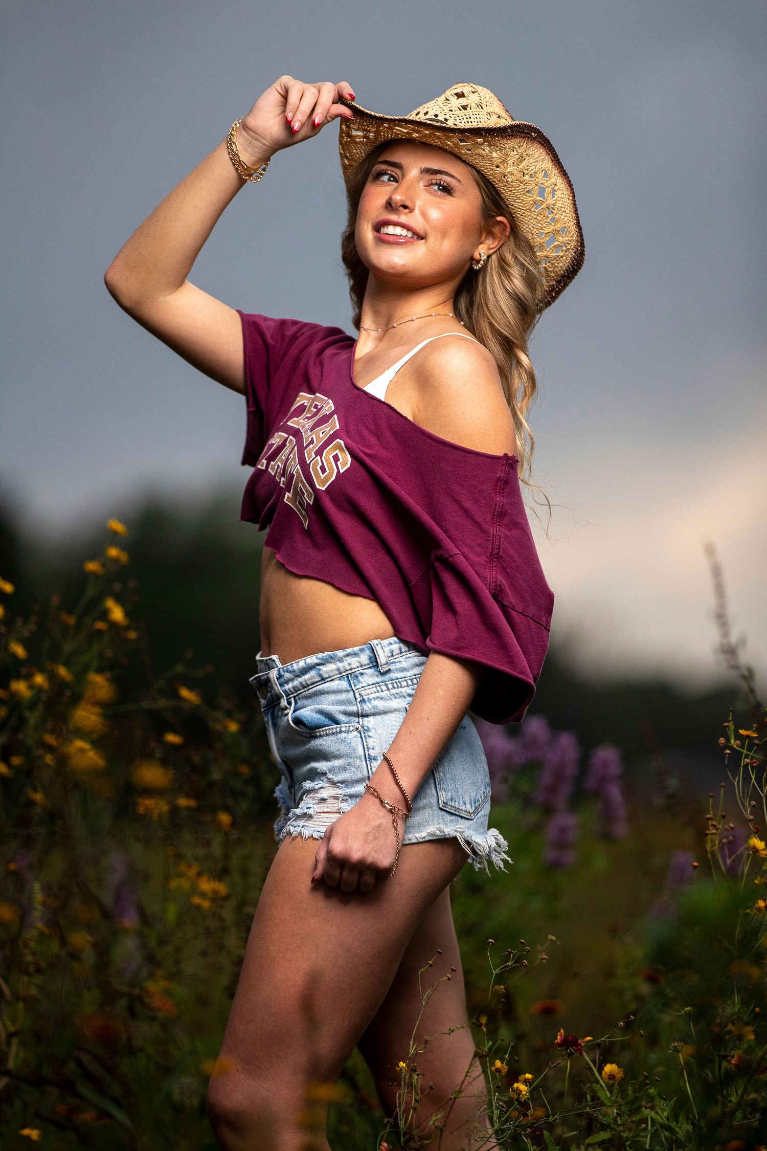 Summer portrait of person in cowboy hat and denim shorts among wildflowers at sunset.