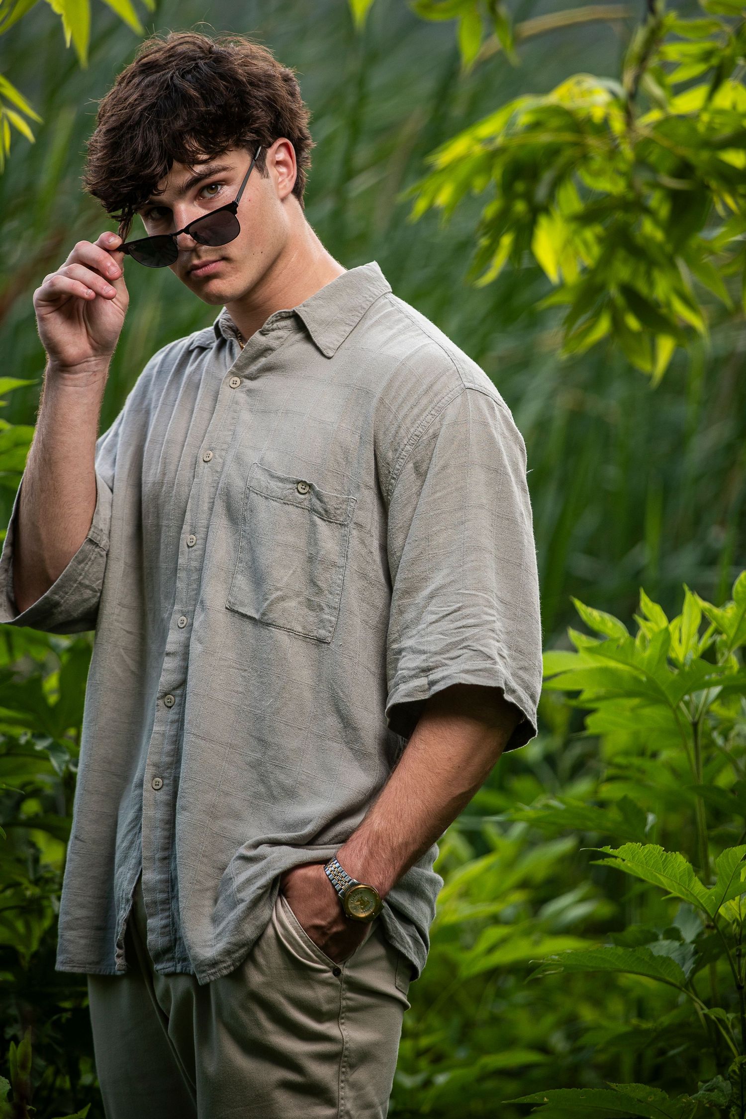 Casual portrait of person in grey shirt against green foliage background.