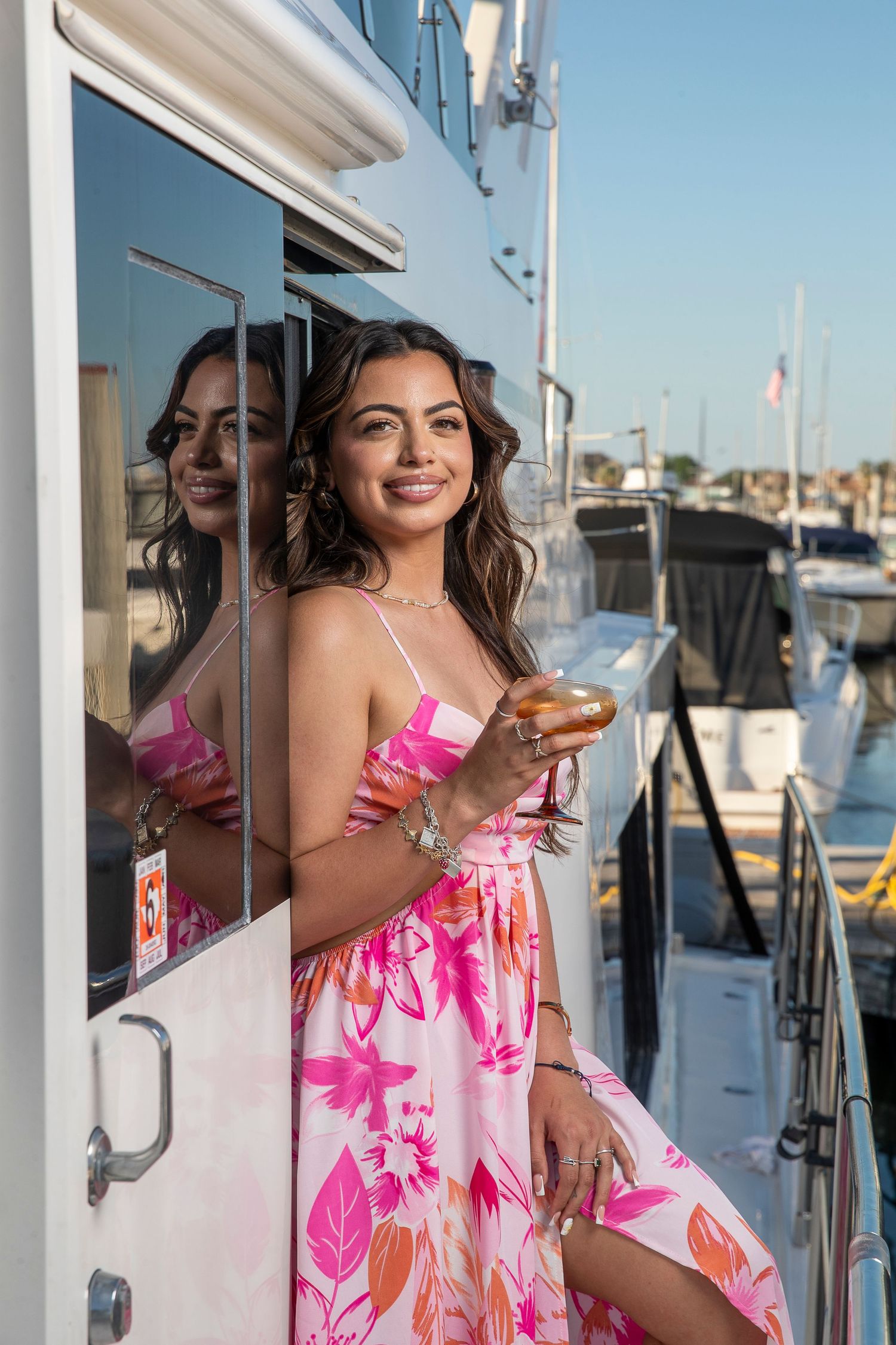 Person in floral pink sundress posing on yacht deck with marina in background.