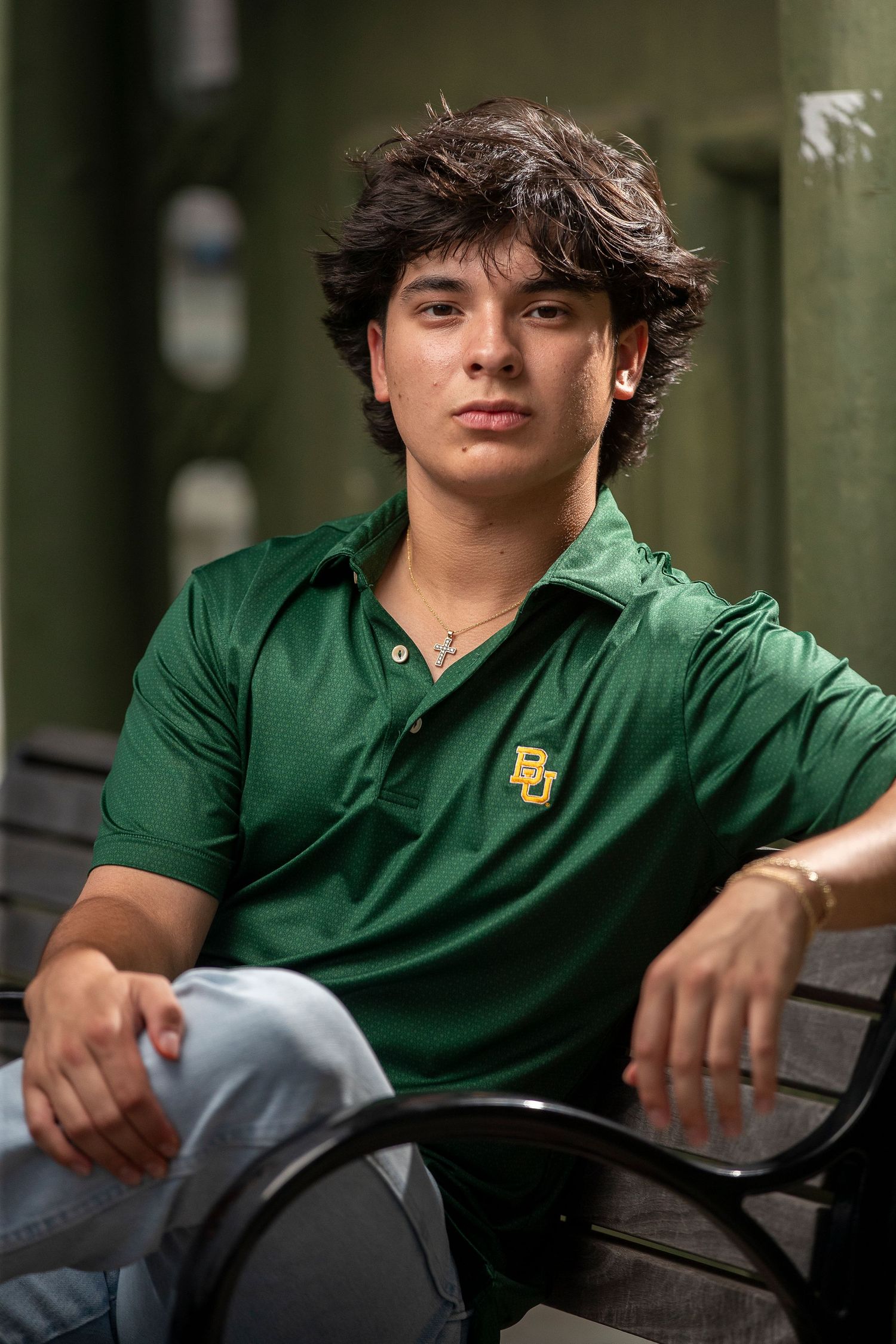 Student in green Baylor University polo shirt relaxing on outdoor bench.