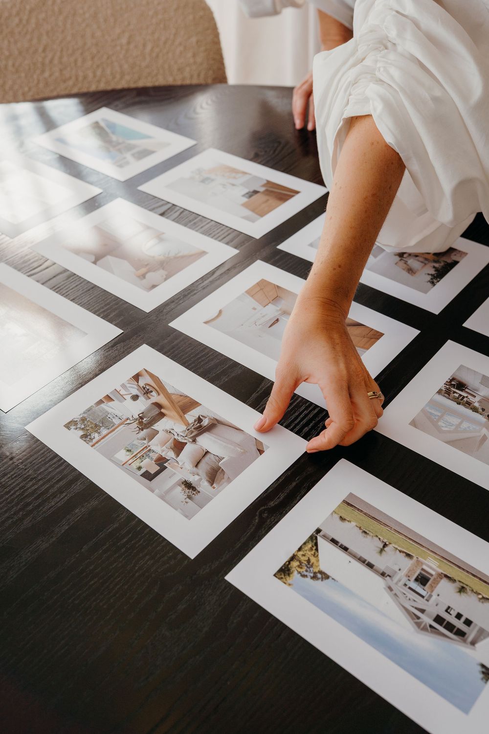 Hands arranging photo prints on a dark surface while organizing a photography album layout.