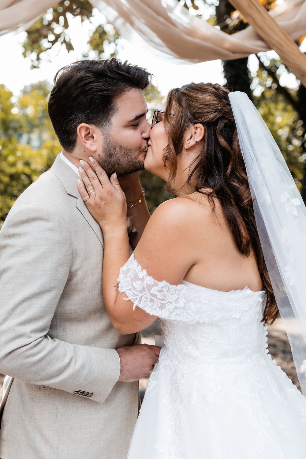 A romantic wedding kiss between newlyweds with the bride in white lace and groom in light gray suit.