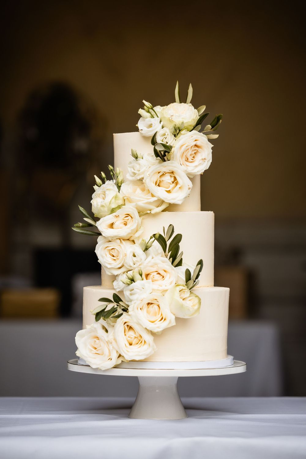 White two-tier wedding cake decorated with cascading peach garden roses on a white pedestal stand.