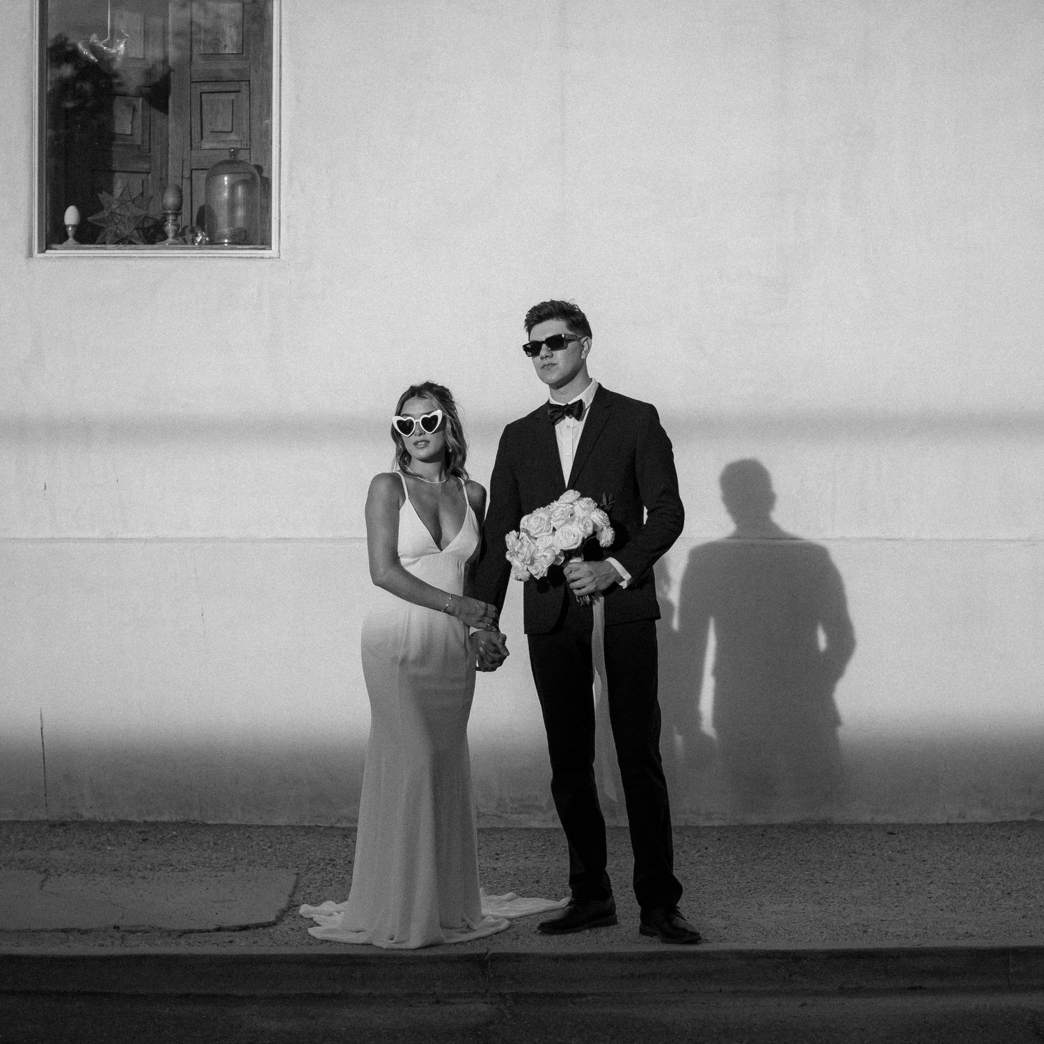 Artistic black and white wedding photos with dramatic shadows against white wall.