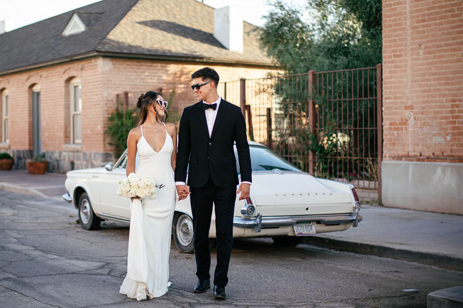 Wedding photography sequence showing couple walking along brick buildings and vintage cars.