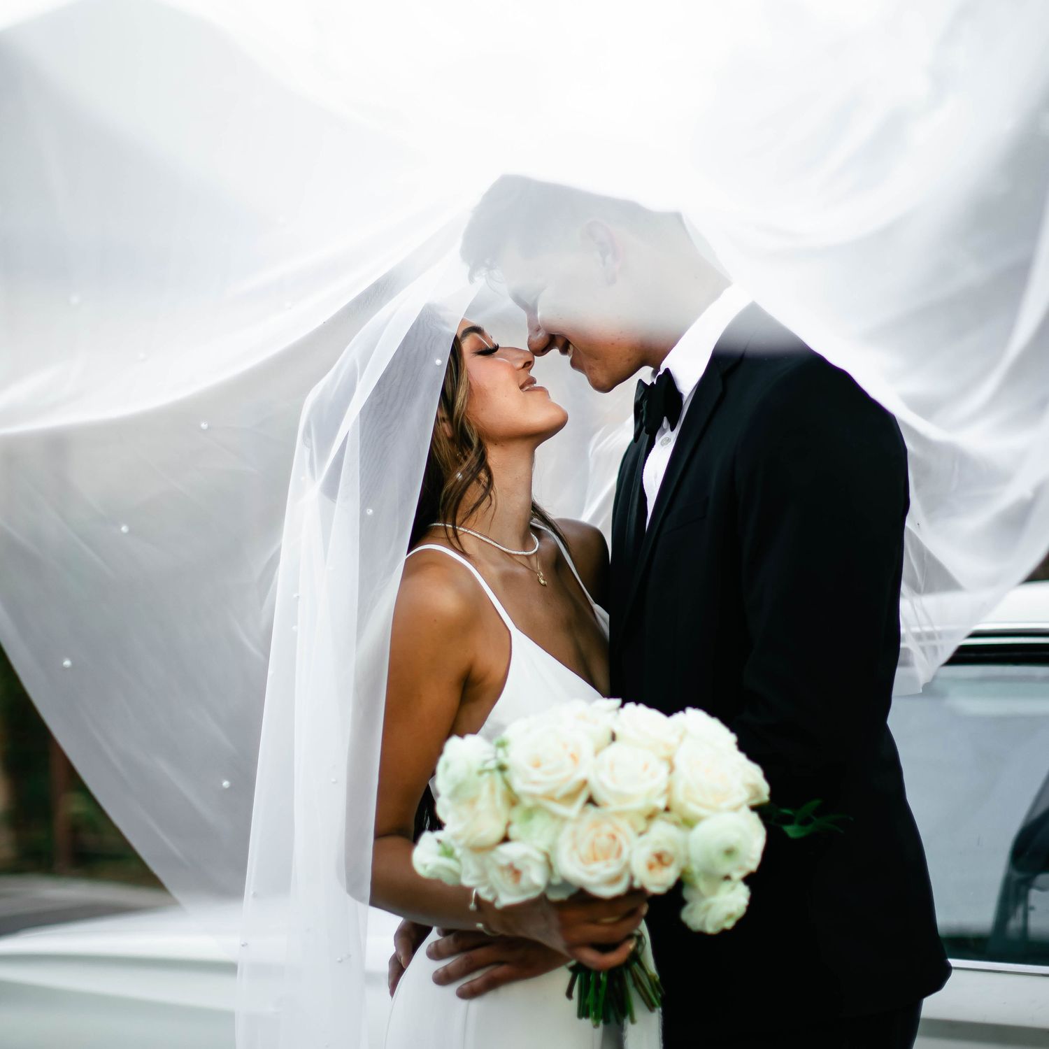 Romantic wedding portraits with flowing veil and white bouquet against soft lighting.
