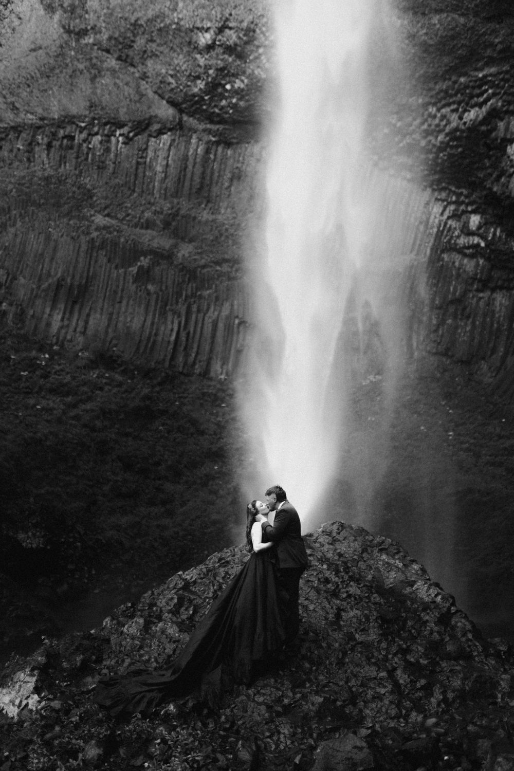 Dramatic waterfall scene with figures in dark clothing positioned on rocky outcrop.