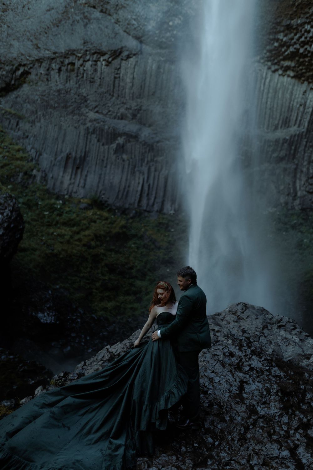 Intimate scene unfolds before dramatic waterfall backdrop on rocky ledge.