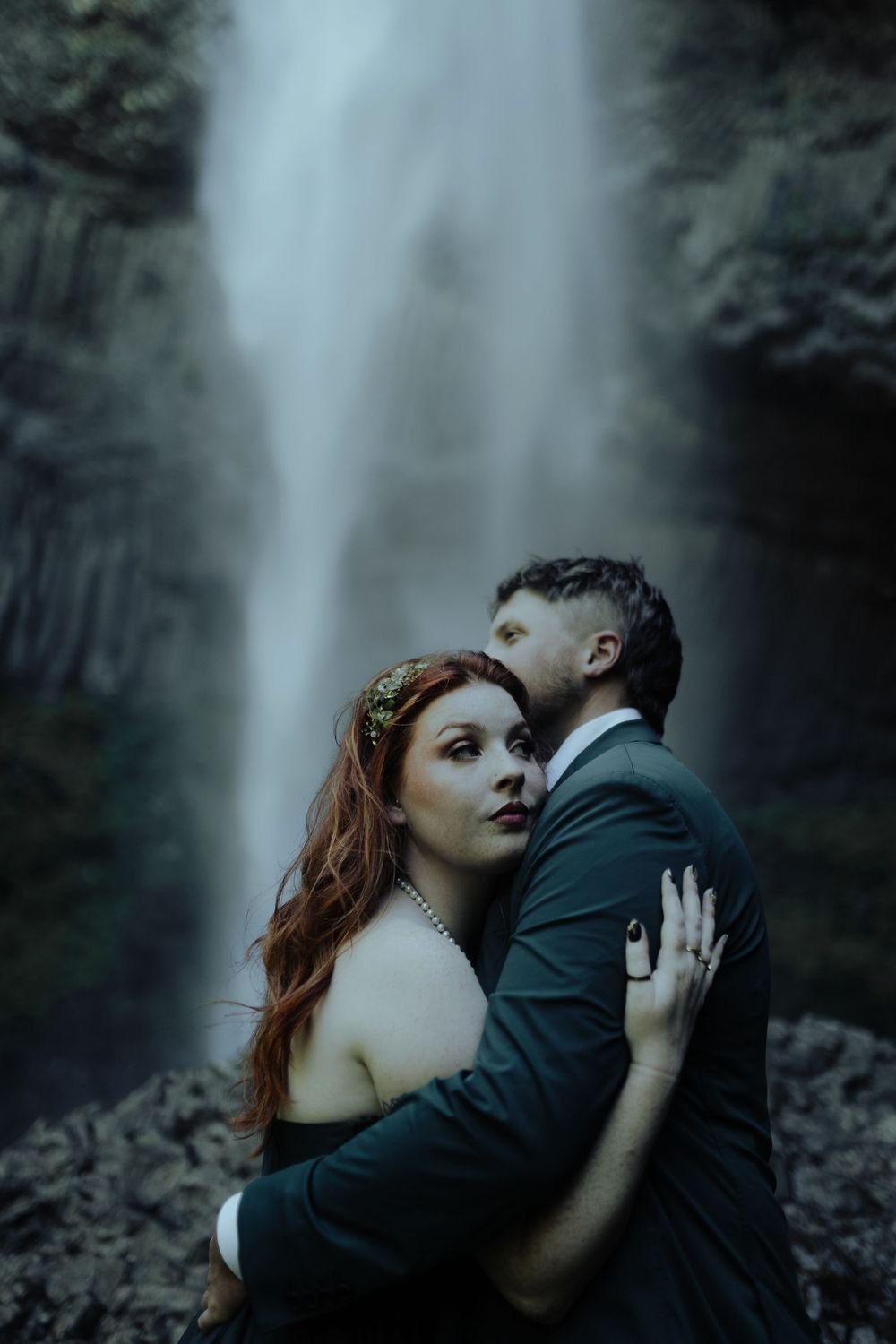Romantic portrait session with waterfall backdrop in moody lighting.
