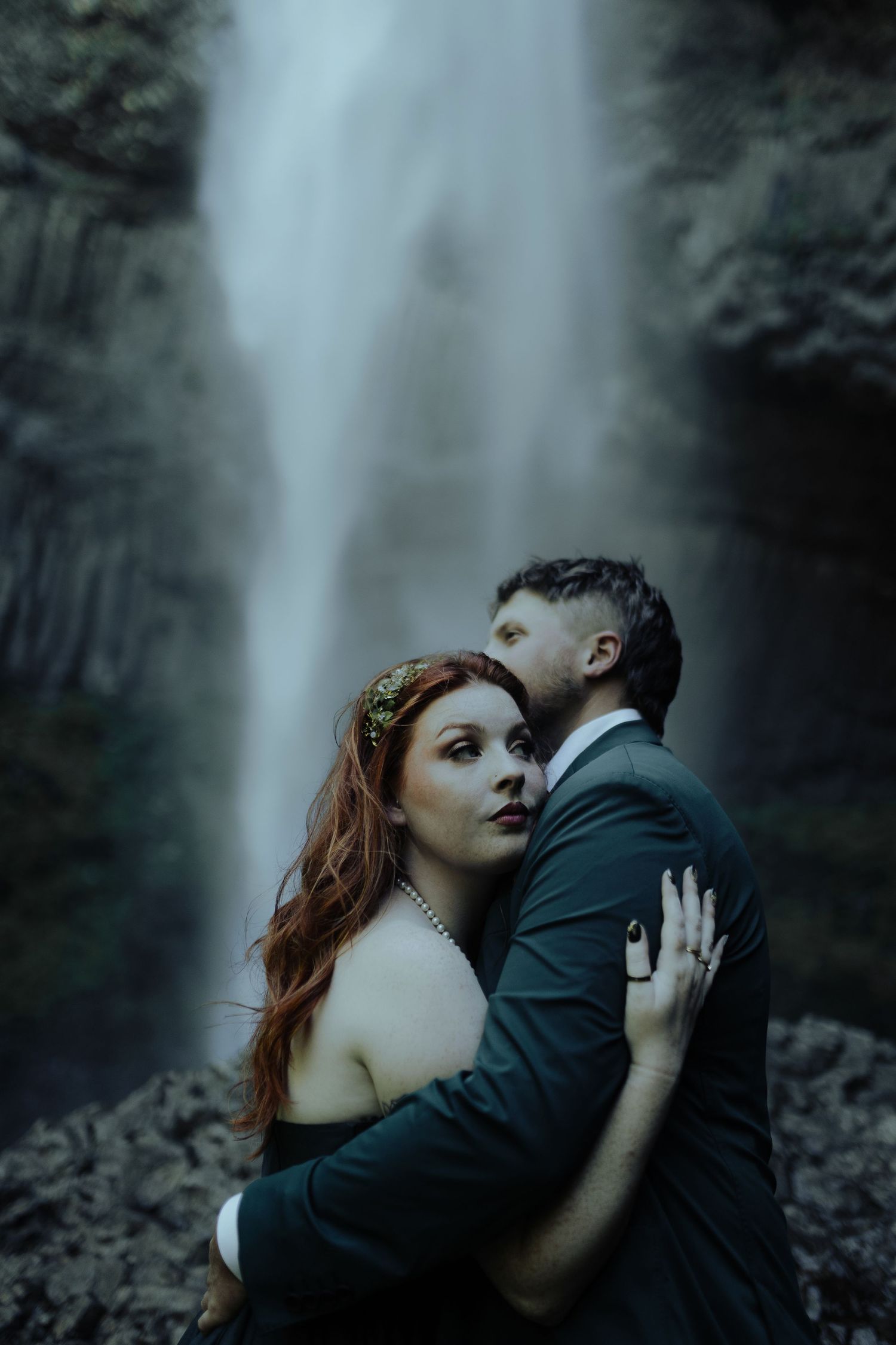 Romantic portrait session with waterfall backdrop in moody lighting.