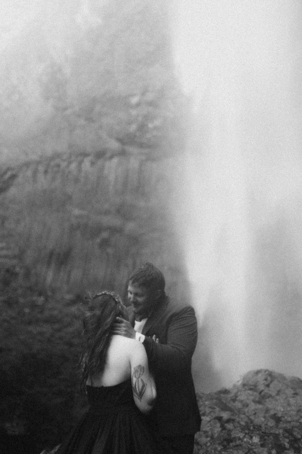 A black and white photo captures an intimate moment near a misty waterfall.