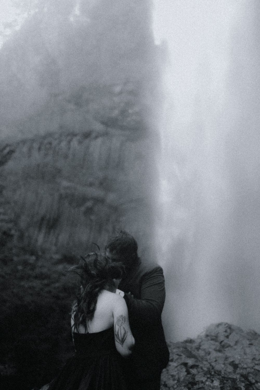 A black and white photograph shows a tender moment against a cascading waterfall backdrop.