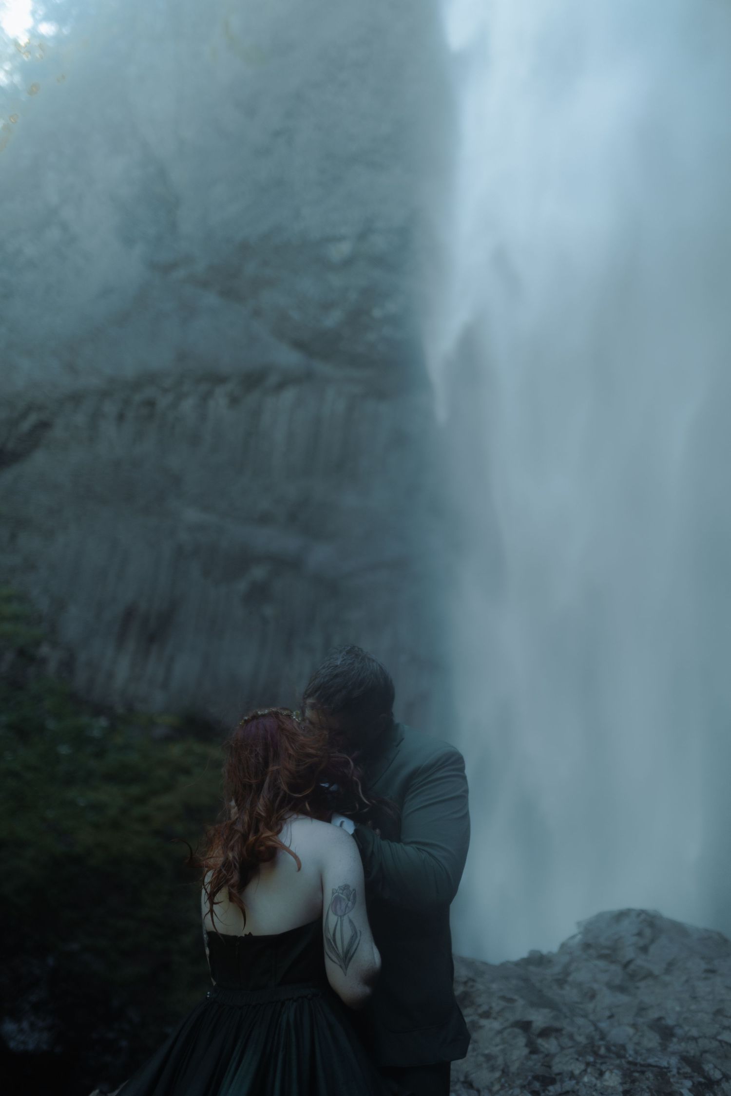 A couple shares an intimate moment in front of a majestic waterfall.