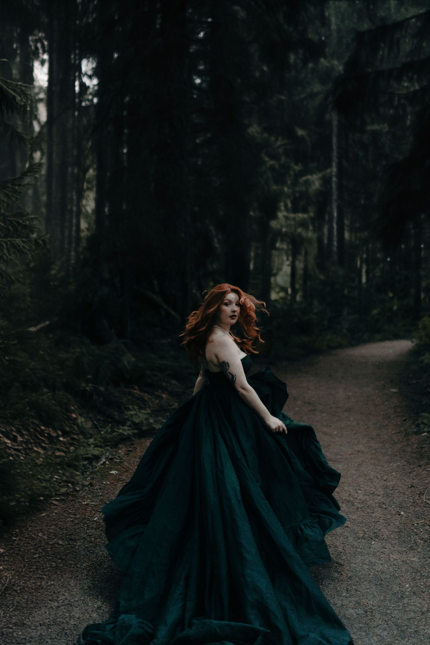 A flowing black dress sweeps dramatically along a forest path.