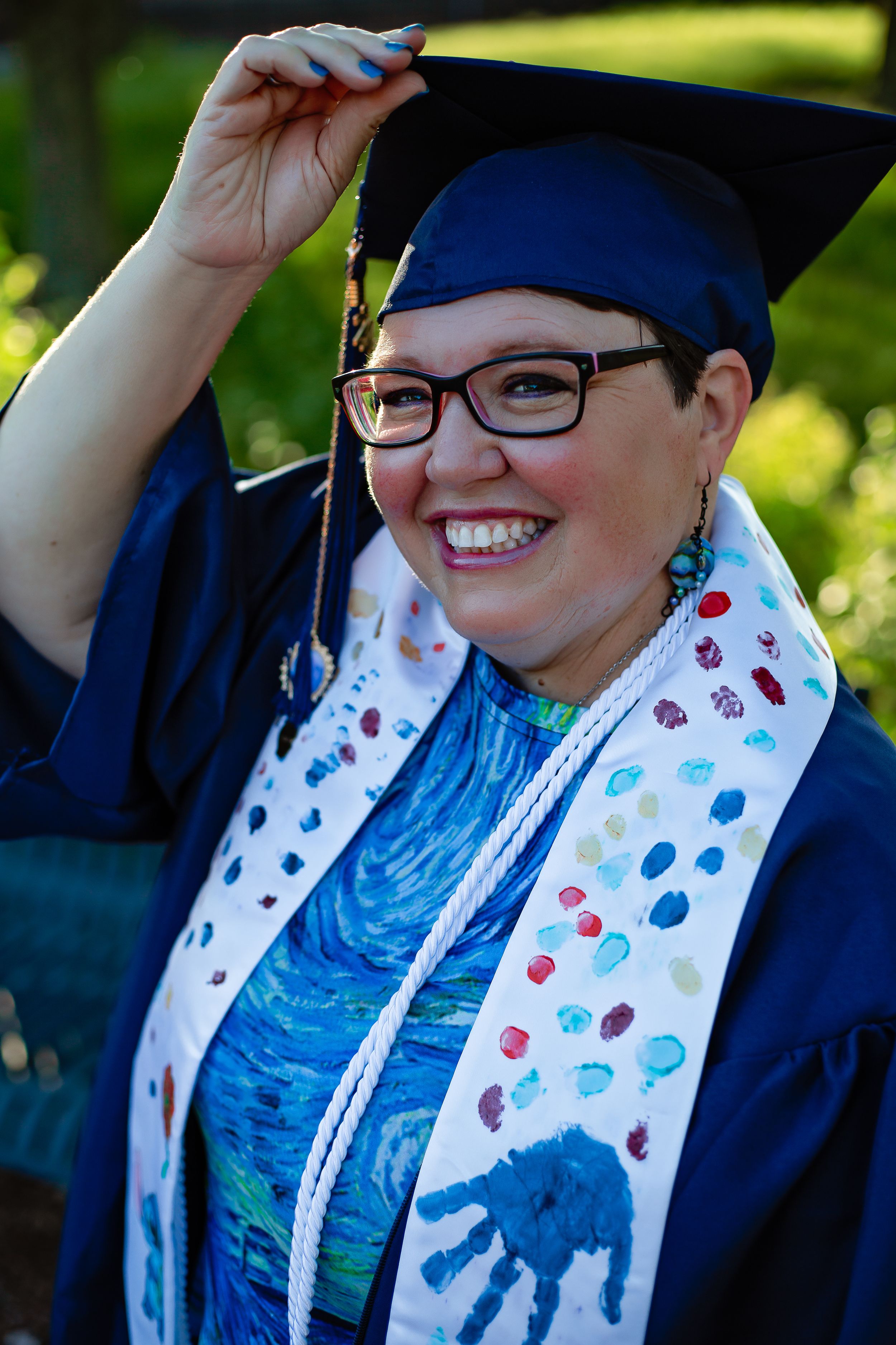 Graduate wearing decorated cap and gown with patterned stole at graduation ceremony.