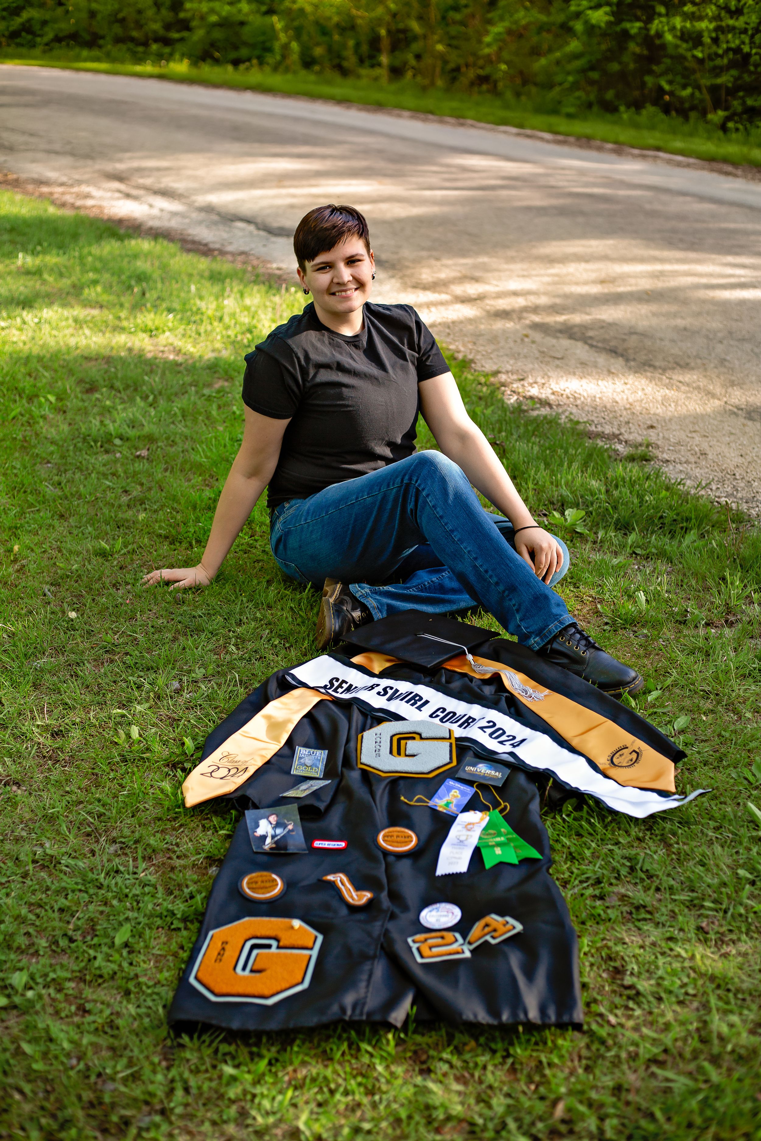 Graduate displays decorated graduation gown with pins and letters on grass.