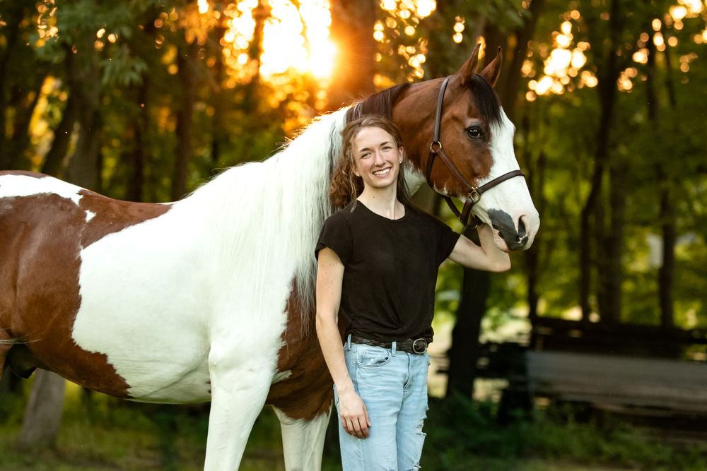 An equestrian photographer standing next to her half-arabian show horse, smiling at the camera