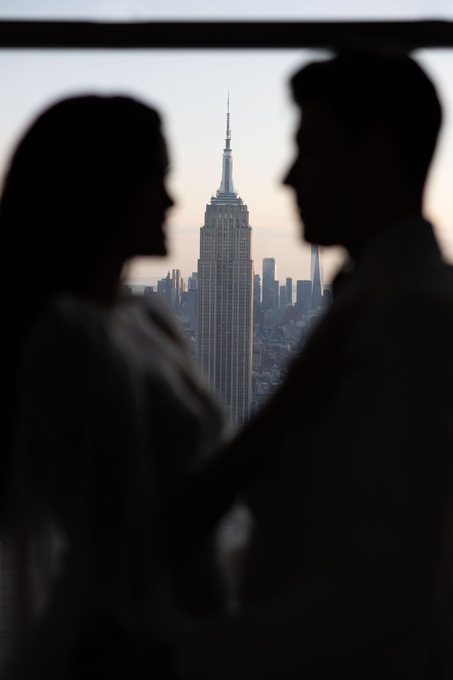 Silhouetted couple standing with Empire State Building visible in background through window.