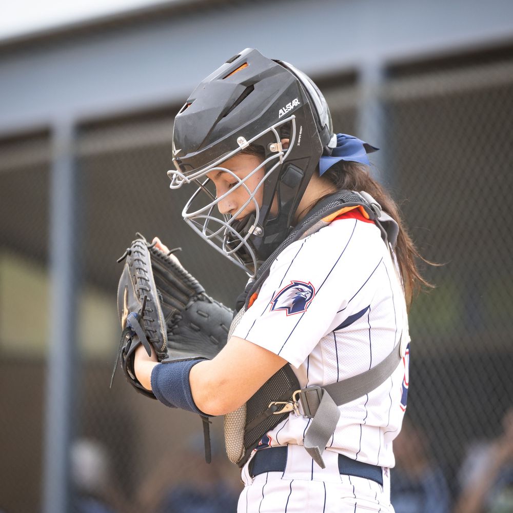 Female softball catcher in helmet and chest gear reviews signals during a game.