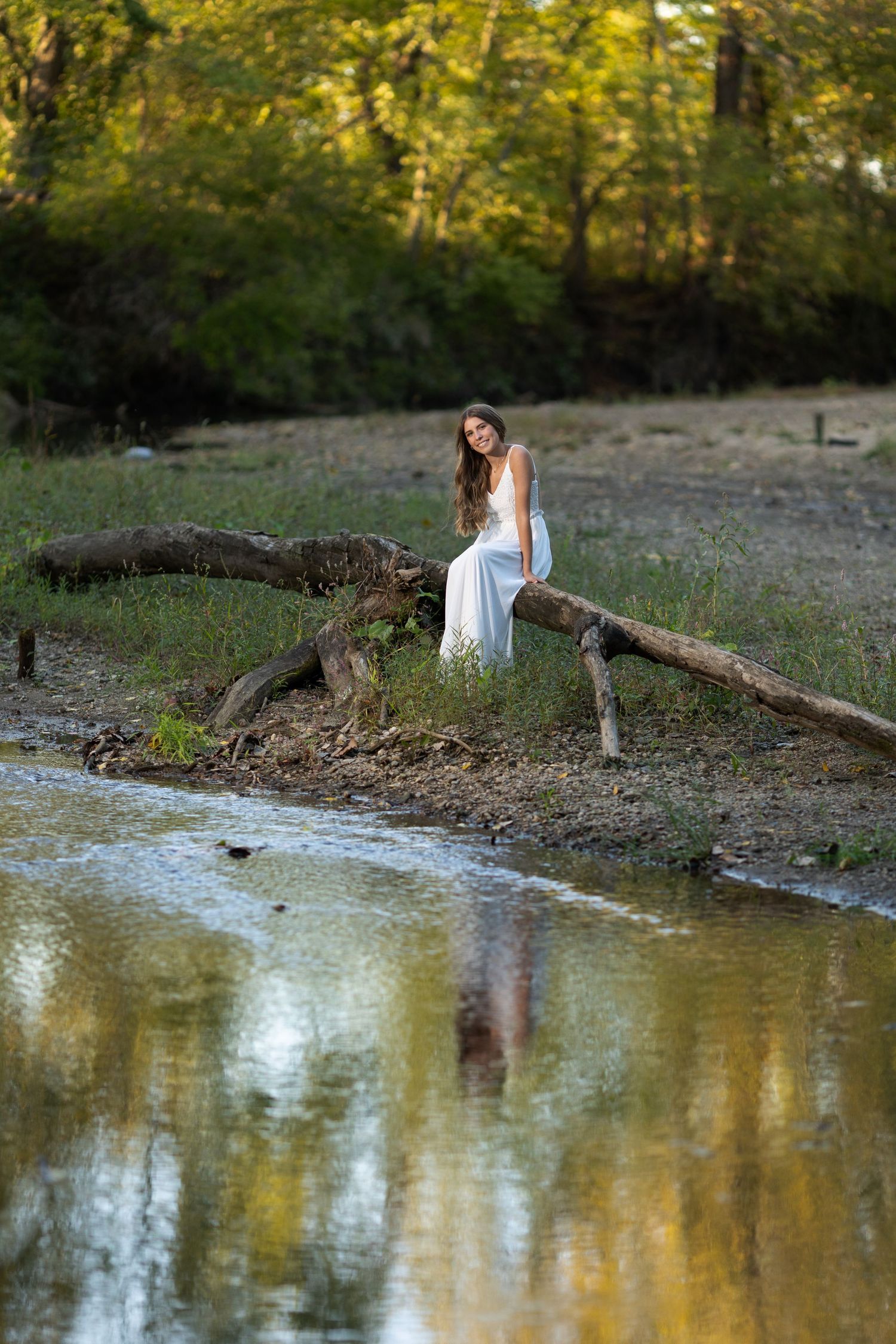 Young lady posing on a log over the creek water.