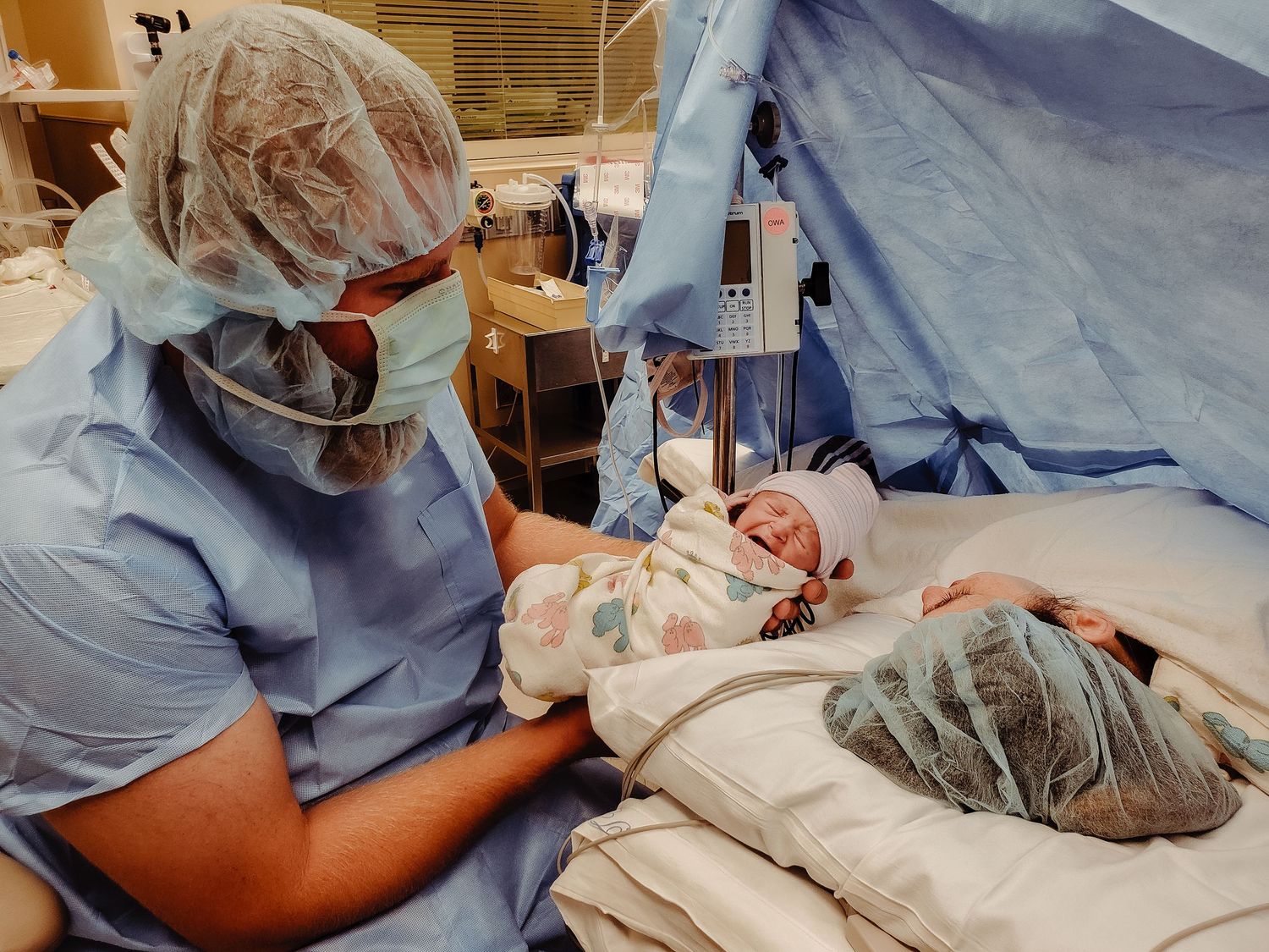 Healthcare worker in scrubs attending to newborn baby in hospital setting.