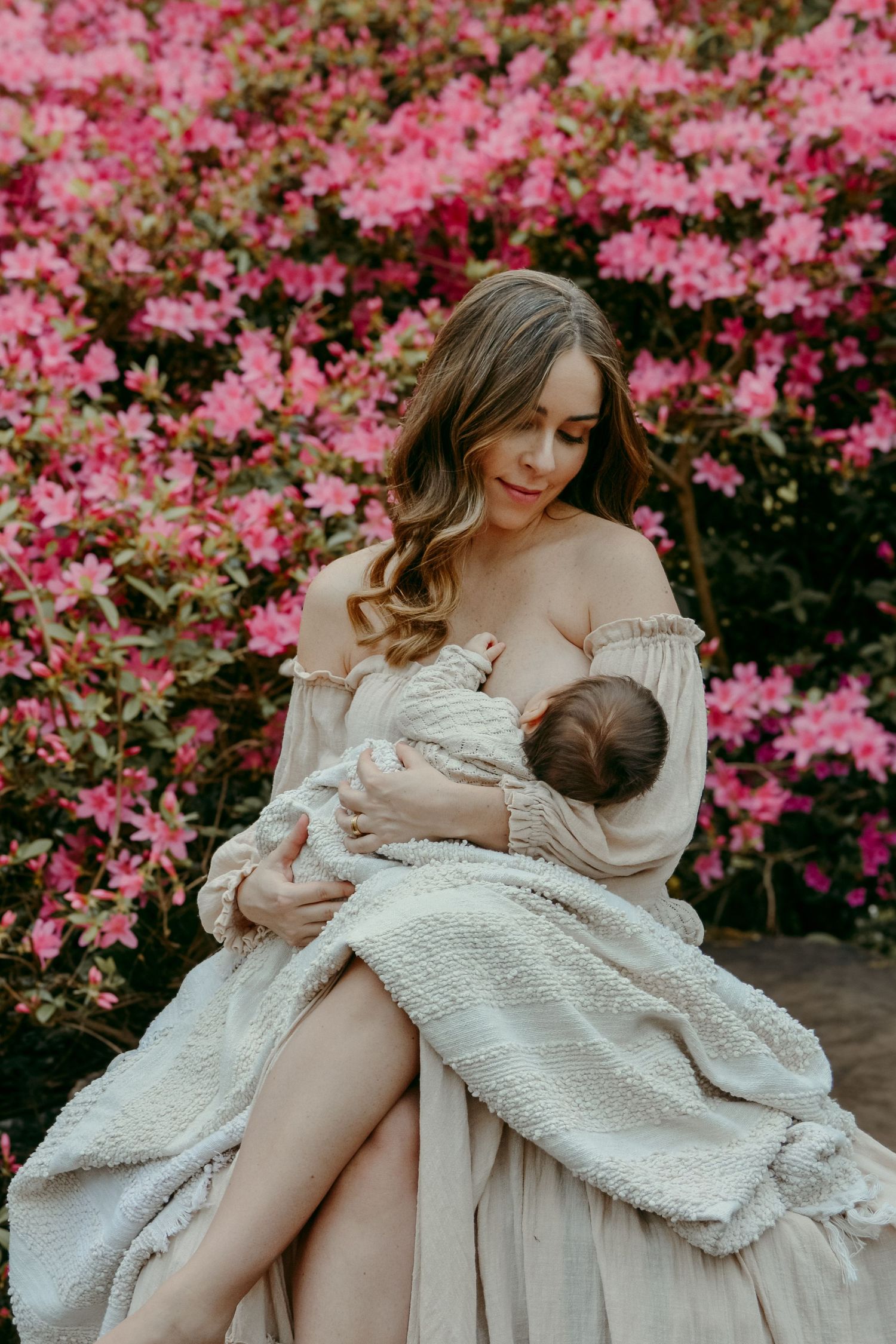 A dreamy portrait against blooming pink azaleas showing a nurturing moment with an infant.