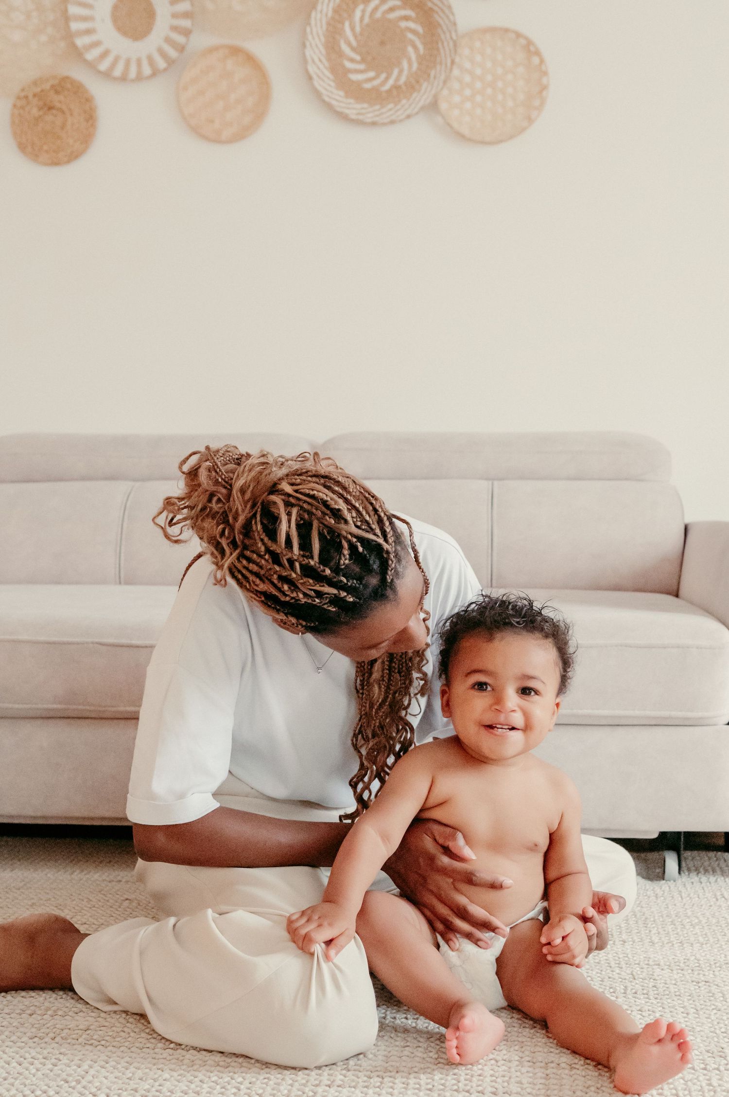 An intimate indoor portrait showing a tender moment between parent and baby on a gray couch.